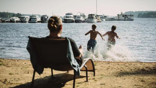a man sitting in a chair on a beach with three boys in the water at Sahanlahti Resort in Puumala