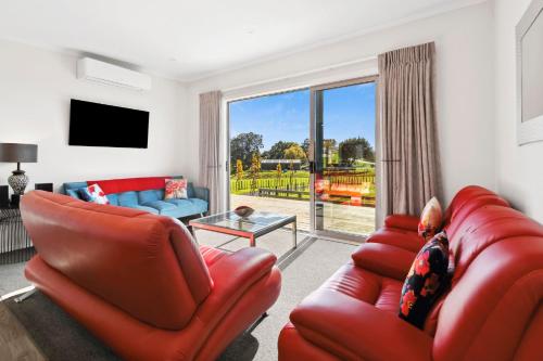 a living room with red leather furniture and a sliding glass door at Country Comfort - only 10 minutes from Hamilton CBD in Hamilton