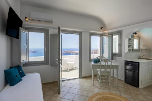 a living room with a table and a kitchen with windows at Ilioperato Hotel in Imerovigli