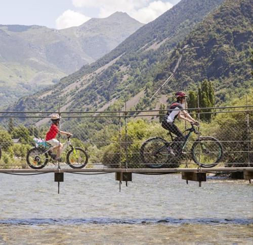 two people riding bikes on a bridge over water at Hostal La Plaça in Erill la Vall