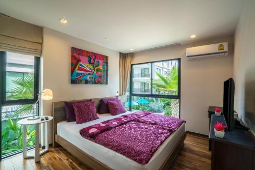 Schlafzimmer mit einem Bett mit lila Kissen und einem TV in der Unterkunft Apartments in The Title Beach Rawai in Rawai Beach