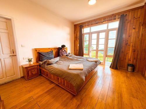 a person sitting on a bed in a room with a large window at Young Monk Hostel & Cafe Dharamkot in McLeod Ganj