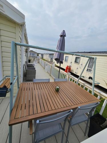 a wooden table and chairs on a balcony with an umbrella at Robins Sunset Holiday Home in Seasalter