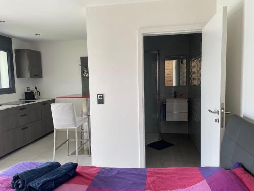 a bedroom with a bed and a kitchen with a chair at Au Chant des Grillons - studio ensoleillé en Gruyère in Estavannens-Dessous