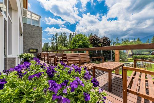 a deck with wooden chairs and purple flowers at Hotel Lesana in Vysoké Tatry