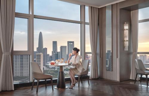 a woman sitting at a table in a room with a view at The Azure Ningbo, Vignette Collection in Ningbo