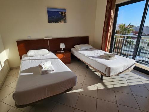 deux lits dans une chambre avec une grande fenêtre dans l'établissement Jardins de Pera vila M, à Pêra