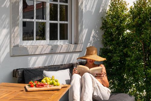 a woman wearing a straw hat reading a book on a patio at Sesimbra Cozy House BBQ & Terrace - MADA HOUSE's in Sesimbra