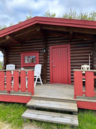 a cabin with red doors and white chairs on a deck at Grasbakken hytteutleie in Nesseby