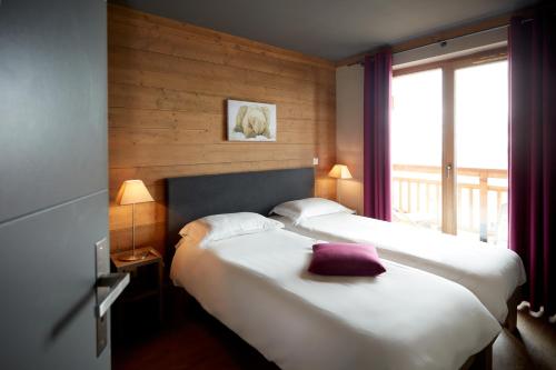 two beds in a hotel room with a window at CGH Résidences & Spas les Chalets du Soleil Contemporain in Les Menuires