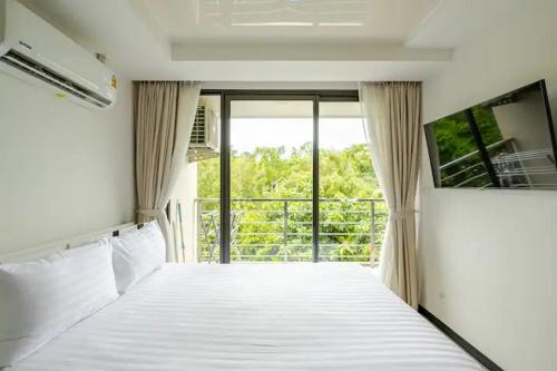 1 dormitorio con cama blanca y balcón en Room 402 Rawai Beach Condo, en Nai Harn Beach