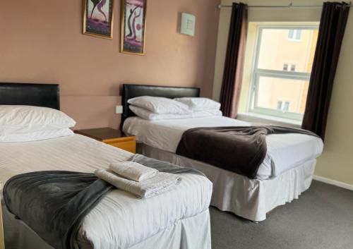 two beds in a hotel room with a window at The Oakland Hotel in Woodham Ferrers