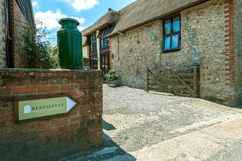 a building with a green trash can on a brick wall at Berehayes Cottages in Whitchurch Canonicorum
