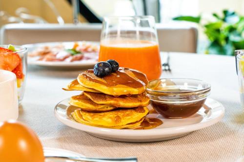 a plate of pancakes with syrup and a glass of orange juice at Enjoy Garda Hotel in Peschiera del Garda