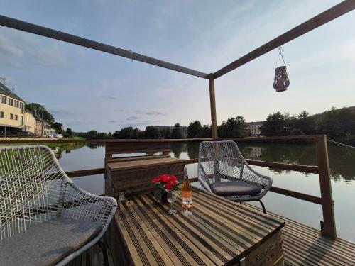 a deck with two chairs and a table with flowers on it at Houseboat Meuse in Vireux-Wallerand