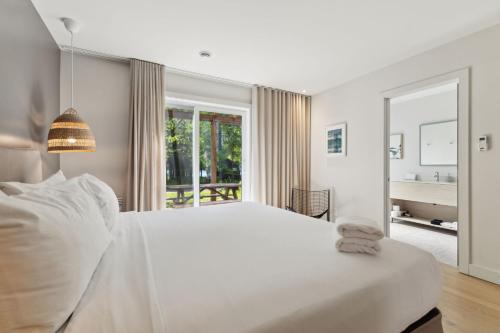 a white bedroom with a large bed and a large window at Suites du Lac Moore by Manitonga in Mont-Tremblant