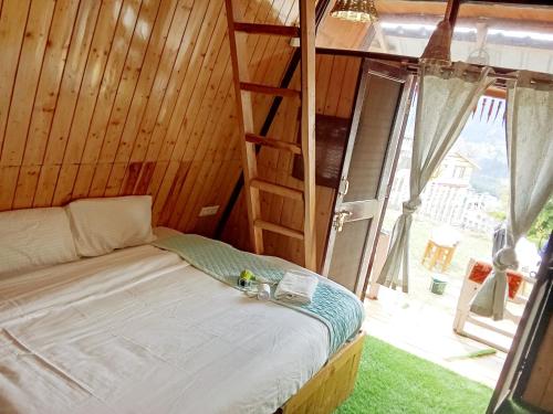 a bed in a wooden room with a large window at Treehouse for couple nr mall road in Manāli