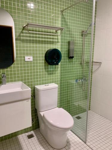 a green tiled bathroom with a toilet and a shower at The Moment Hostel Dulan in Donghe