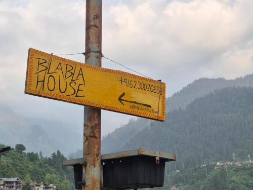 a yellow street sign on a pole with mountains in the background at Blabla House Himachal in Pulga