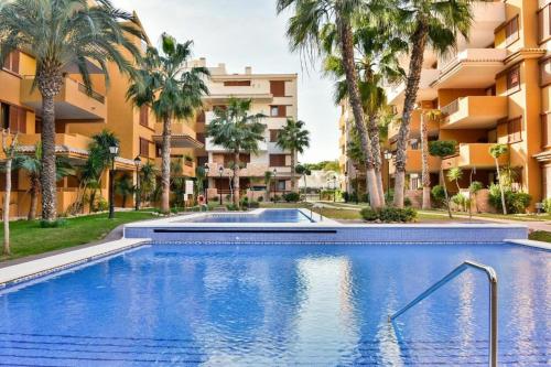 a swimming pool in front of a building with palm trees at CC8 VI by ZANIS in Torrevieja