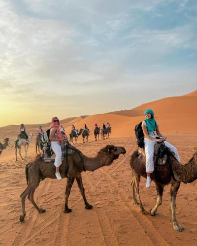 a group of people riding on camels in the desert at Infinity sahara camp in Merzouga