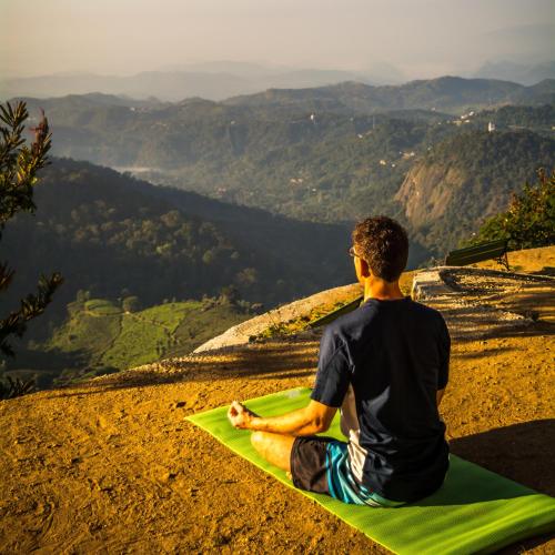 a man sitting on a green yoga mat on a mountain at Blackberry Hills Munnar Nature Resort & Spa in Munnar