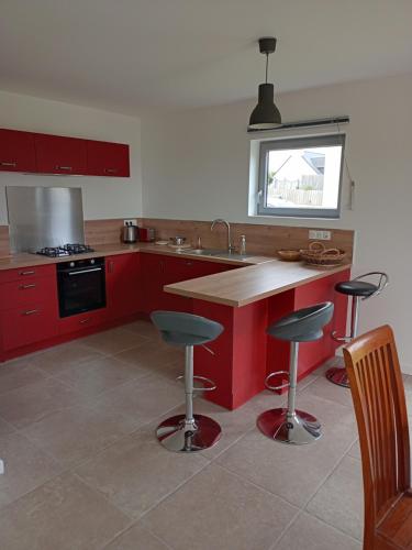 une cuisine avec des placards rouges et un îlot avec des tabourets de bar dans l'établissement Maison vue mer proximité plages, à Plozévet