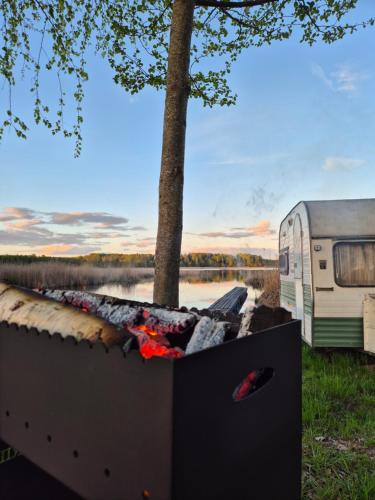 a fire pit next to an rv and a lake at Telšu vieta Sīvera Medniekkrasti 