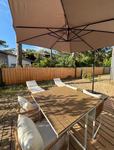 une table en bois avec des chaises et un parasol dans l'établissement Maison neuve Lacanau à 300m de la plage sud et à proximité des golfs, à Lacanau