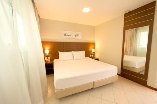 a bedroom with a white bed and a mirror at Quality Hotel Vitória in Vitória