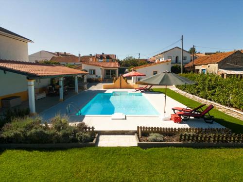 a swimming pool in a yard with two chairs and an umbrella at Casa do Sol - Turismo Rural - Nazaré Alcobaça in Cos
