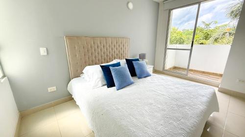 a bedroom with a bed with blue pillows and a window at Hermoso Apartamento con Pisicina 3 Habitaciones I214 in Montería