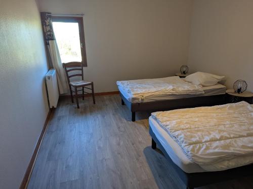 two beds in a room with a chair and a window at Gîte confortable dans l'ancien presbytère de Futeau, 3 chambres, jardin, WiFi, entre Verdun et Châlons - FR-1-585-13 in Futeau