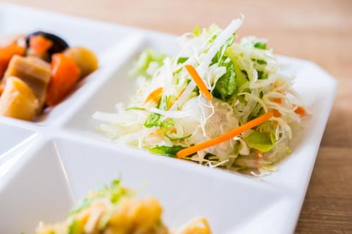 a white plate of food with cabbage and carrots at SUPERHOTEL Matsumoto Oshiroguchi in Matsumoto