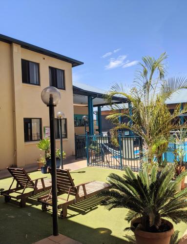 a patio with chairs and palm trees in front of a building at Ningaloo Club Backpackers in Coral Bay