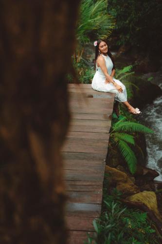 a woman sitting on a wooden bridge in the forest at Glamping tent in Pelaga Eco Park in Patjung