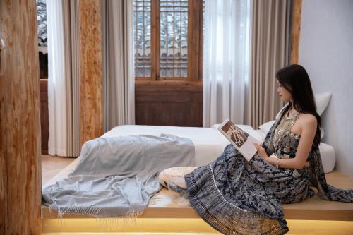 a woman sitting on a bed reading a book at Shanyeji Garden Resort Panorama Hotel in Xinping