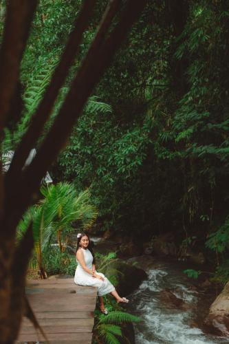 a woman sitting on a wooden bridge in a forest at Glamping tent in Pelaga Eco Park in Patjung