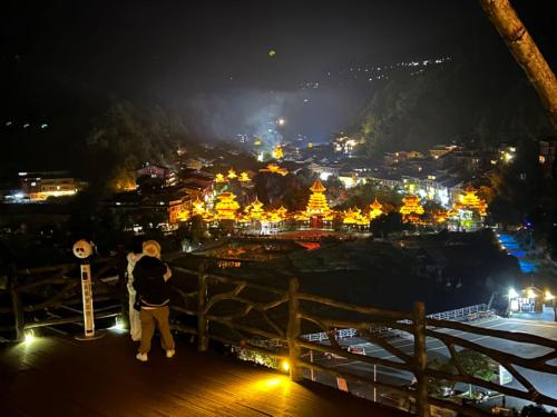 a couple standing on a bridge looking at a city at night at Shanyeji Garden Resort Panorama Hotel in Xinping