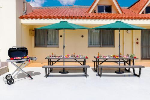two picnic tables and umbrellas in front of a house at 恩納村飲食店の中心地ビーチまで徒歩3分最大12名貸切コーディアルステイ in Fuzuchi