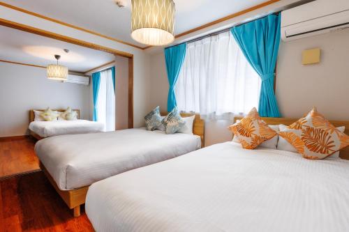 two beds in a room with blue curtains at 恩納村飲食店の中心地ビーチまで徒歩3分最大12名貸切コーディアルステイ in Fuzuchi