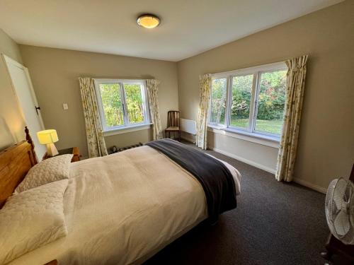 a bedroom with a large bed and two windows at 25 Leamington Street in Hanmer Springs