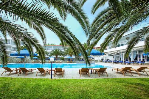 a pool with chairs and palm trees next to a building at Xenios Port Marina Hotel in Pefkohori