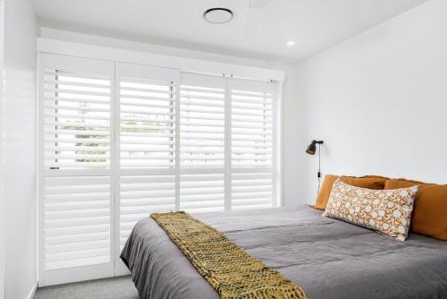 a bedroom with a bed with white shutters on the window at Sanctuary Spaces - Lomani Six in Byron Bay
