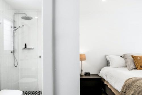 a white bedroom with a shower and a bed at Sanctuary Spaces - Lomani Six in Byron Bay