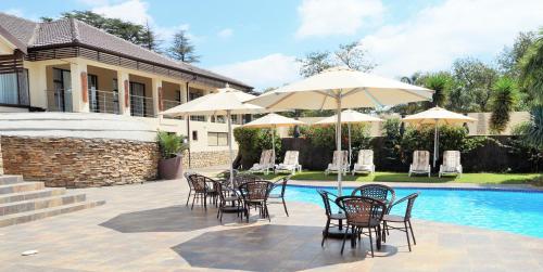 eine Terrasse mit Stühlen und Sonnenschirmen neben einem Pool in der Unterkunft Ecotel Premier Lodge & Conference Centre in Benoni