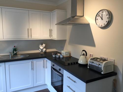 a kitchen with white cabinets and a clock on the wall at Bruce's Cottage in Stirling