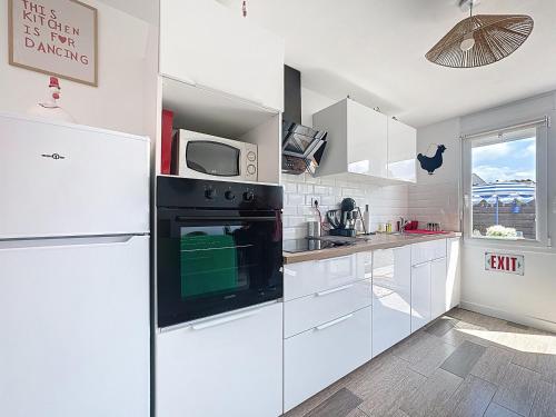 une cuisine blanche avec un réfrigérateur et un micro-ondes dans l'établissement Maison colorée - 2 chambres - À 5 min de la mer, à Plérin