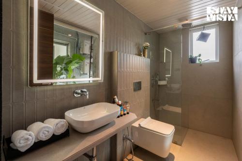 a bathroom with a sink and a toilet and a mirror at StayVista at Avyanna Villa - BBQ & Pool in Kārli