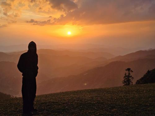 a person standing on a hill looking at the sunset at Boom shiva camps in Mandi